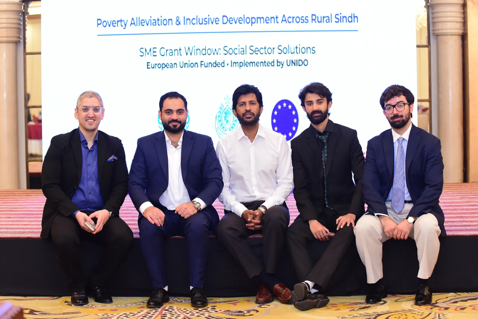 Ali Ahmed with his Digitara colleagues at the UNIDO PAIDAR founder event in Karachi, seated in front of the programme backdrop reading “Poverty Alleviation & Inclusive Development Across Rural Sindh — SME Grant Window: Social Sector Solutions — European Union Funded, Implemented by UNIDO”.
